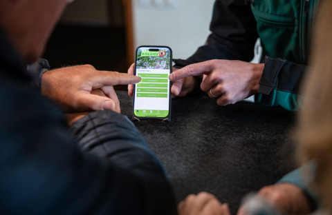 People using the Roland campsite app on a smartphone at a table in Limburg, Netherlands holiday park.