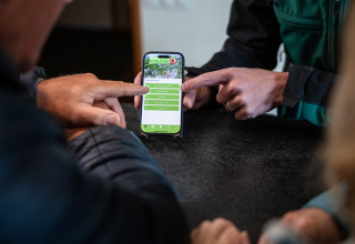 Persone usano l’app del campeggio Roland su uno smartphone a un tavolo in Limburg, Paesi Bassi.