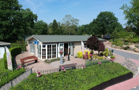 Bright holiday cottage with garden benches and lush greenery at Campsite Roland in Limburg, Netherlands, sunny day.