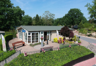 Casa vacanze luminosa circondata da fiori e panchine al campeggio Roland in Limburg, Paesi Bassi, giornata soleggiata.