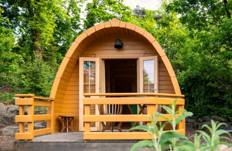 Ein kleines Holz-Pod-Haus mit Veranda, umgeben von grünen Bäumen und Büschen in der Natur.