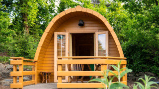 Ein kleines Holz-Pod-Haus mit Veranda, umgeben von grünen Bäumen und Büschen in der Natur.