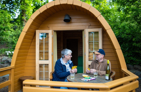 Two people play cards on the deck of a wooden Pod tiny house at Campsite Roland in the Netherlands.