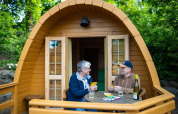 Two people play cards on the deck of a wooden Pod tiny house at Campsite Roland in the Netherlands.