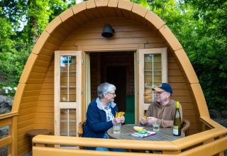 Two people play cards on the deck of a wooden Pod tiny house at Campsite Roland in the Netherlands.