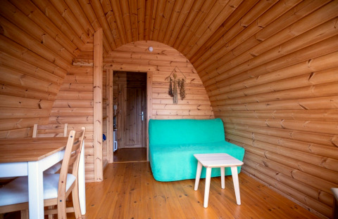 Holzinterieur eines Tiny House Pod auf dem Campingplatz Roland in den Niederlanden mit grüner Couch.