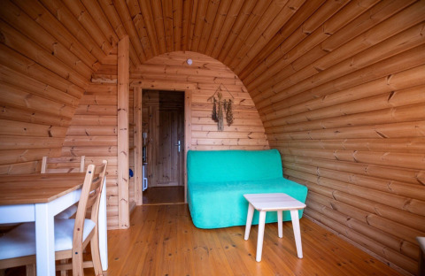 Wooden interior of a Pod tiny house at Campsite Roland in the Netherlands, featuring a green sofa.