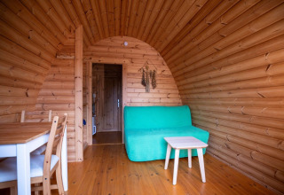 Wooden interior of a Pod tiny house at Campsite Roland in the Netherlands, featuring a green sofa.