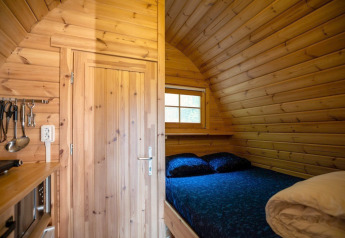 Intérieur en bois d'une tiny house avec lit et ustensiles de cuisine au Pod, Campsite Roland, Pays-Bas.