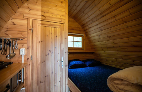 Wooden tiny house interior with a bed and kitchen utensils at Pod, Campsite Roland, Netherlands.