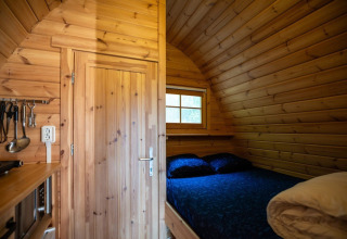Wooden tiny house interior with a bed and kitchen utensils at Pod, Campsite Roland, Netherlands.
