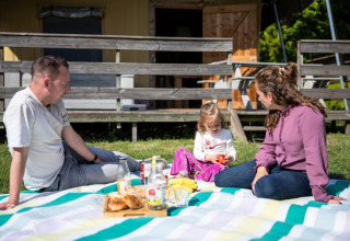 Famiglia fa un picnic su una coperta davanti a una tenda safari al Campeggio Roland nei Paesi Bassi.