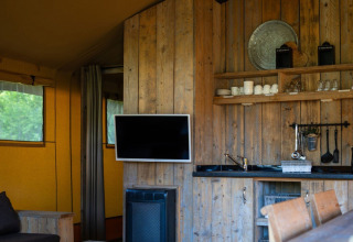 Interior of a safari tent at Campsite Roland in the Netherlands, showing wood kitchen, shelves, and TV.