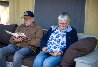 Due anziani si rilassano nella tenda safari al Campeggio Roland, Paesi Bassi, leggendo e usando un tablet.