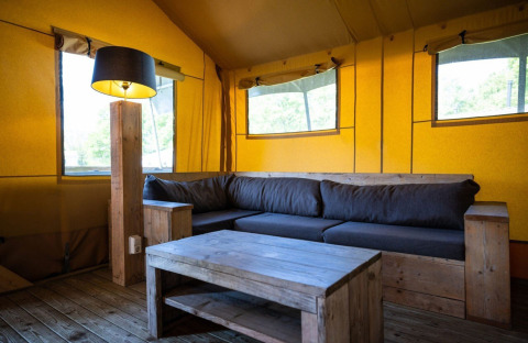 Innenraum eines Safari-Zeltes auf Campingplatz Roland in den Niederlanden mit Holzmöbeln und Sofa.