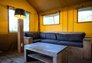 Interiør af safari-telt på Campsite Roland i Holland med træmøbler og grå sofa i hyggelig atmosfære.