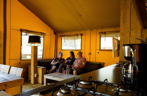 Indvendigt billede af safaritelten på Camping Roland i Holland med tre personer, der slapper af.