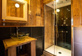 Bathroom in a safari tent at Campsite Roland in the Netherlands, featuring wood walls, glass sink, and shower.