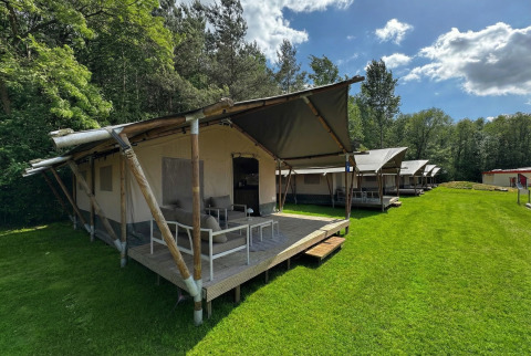 Tentes lodge safari modernes sur pelouse avec terrasse, adossées à une forêt, idéales pour glamping.