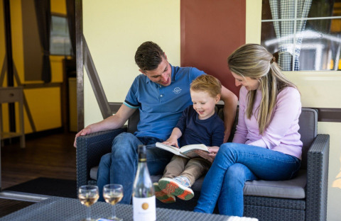 Familie sitzt auf einem Sofa und liest gemeinsam ein Buch im Fachwerkzelt auf Camping Roland, Niederlande.