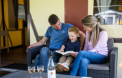 Familie sitzt auf einem Sofa und liest gemeinsam ein Buch im Fachwerkzelt auf Camping Roland, Niederlande.