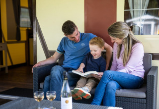 Familie sitzt auf einem Sofa und liest gemeinsam ein Buch im Fachwerkzelt auf Camping Roland, Niederlande.