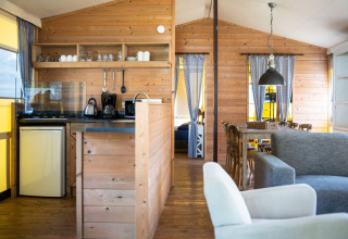 Innenansicht eines gemütlichen Safarizeltes mit Holzwänden, Küche, Esstisch und Sofa auf Camping Roland.