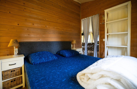 Bedroom in a safari tent with wooden walls, double bed and blue bedding at Campsite Roland in the Netherlands