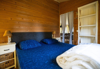 Dormitorio en tienda safari con paredes de madera, cama doble y ropa de cama azul en Camping Roland, Países Bajos
