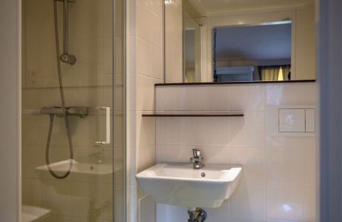 Bagno con lavabo bianco, specchio e doccia in vetro in una tenda safari a graticcio al Camping Roland.