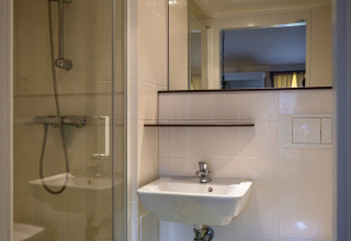 Badezimmer mit weißem Waschbecken, Spiegel und Glasdusche im Fachwerk-Safarizelt auf Camping Roland.