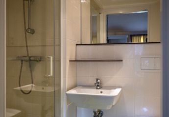 Salle de bain avec lavabo blanc, miroir et douche vitrée sous tente safari à ossature au Camping Roland.