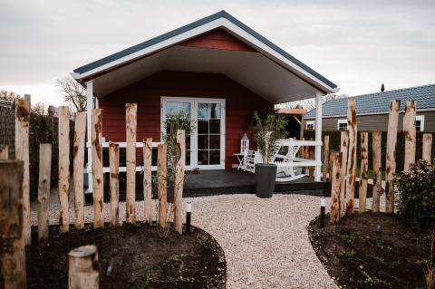 Facciata della Veluwe lounge + sauna lodge con sentiero di ghiaia, staccionata rustica e veranda accogliente.