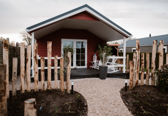 Veluwe lounge + sauna lodge met grindpad, rustiek houten hek, veranda en witte tuinmeubelen buiten.