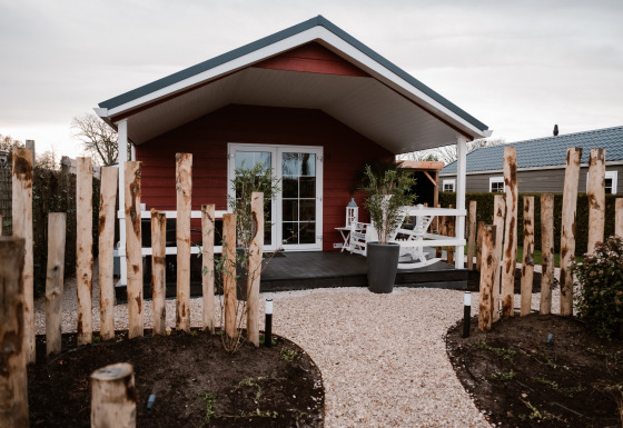 Veluwe lounge + sauna lodge set fra stien, med træhegn, terrasse og komfortable udendørs siddepladser.