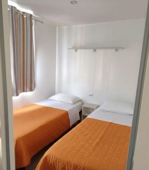 Due letti singoli in una casa mobile al Centro Vacanze San Marino, con copriletti arancioni.