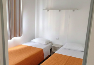 Dos camas individuales en una casa móvil en Centro Vacanze San Marino, con cobertores naranjas.