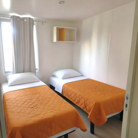 Camera da letto nella casa mobile «Royal» al Centro Vacanze San Marino con due letti singoli e coperte arancioni.