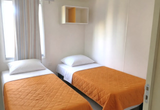 Chambre du mobil-home «Royal» au Centro Vacanze San Marino avec deux lits simples aux couvre-lits orange.