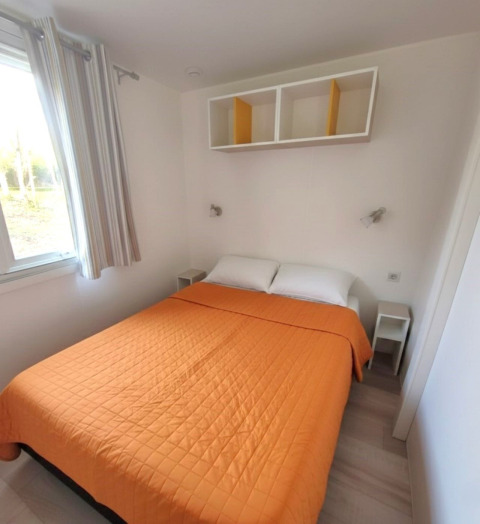 Camera luminosa nel Mobile home «Royal» a Centro Vacanze San Marino, con copriletto arancione e mensole bianche.