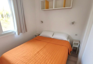 Lyst værelse i Mobile home «Royal» med orange sengelinned, hvide vægge og vindue på Centro Vacanze San Marino.