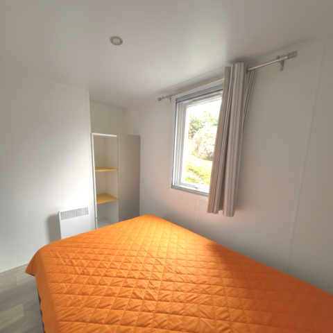 Schlafzimmer im Mobilheim ‚Royal‘ im Centro Vacanze San Marino mit orangefarbener Decke, Fenster und Regal.