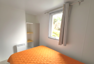 Dormitorio en la casa móvil «Royal» del Centro Vacanze San Marino con colcha naranja y decoración clara.