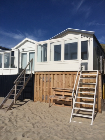 Cabine de plage Strand Dishoek 342, escaliers devant, sable au sol et ciel bleu clair en arrière-plan.