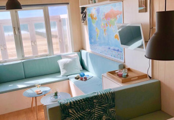 Bright beach cabin interior with pastel seating, world map on the wall, and seaside view from the window.