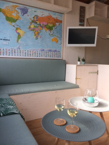 Acogedora zona interior en una cabaña de playa con mapa mundial, TV, plantas y dos copas de vino blanco.