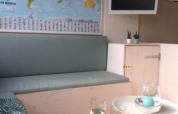 Accogliente zona lounge in cabina sulla spiaggia con mappa del mondo, TV, piante e due bicchieri di vino.