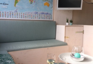 Acogedora zona interior en una cabaña de playa con mapa mundial, TV, plantas y dos copas de vino blanco.
