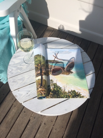 Tavolo rotondo bianco con vino e rivista all’esterno presso Beach sleeping cabin Strand Dishoek 342 nei Paesi Bassi.