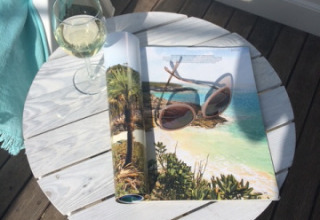 Et hvidt bord med et glas vin og et magasin udendørs på træterrasse ved Beach sleeping cabin Strand Dishoek 342.